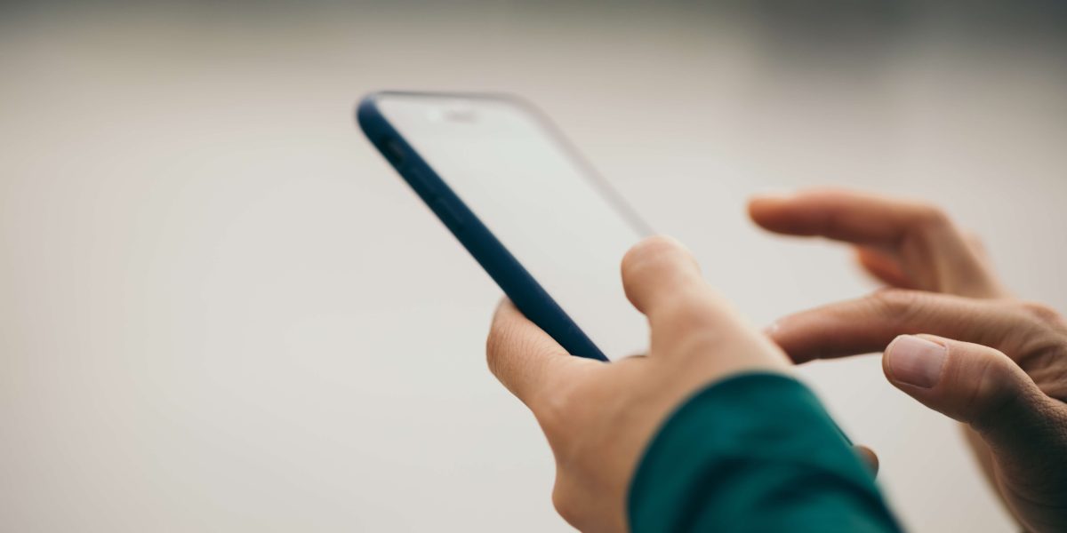 Händer som använder en smartphone mot ljus bakgrund.