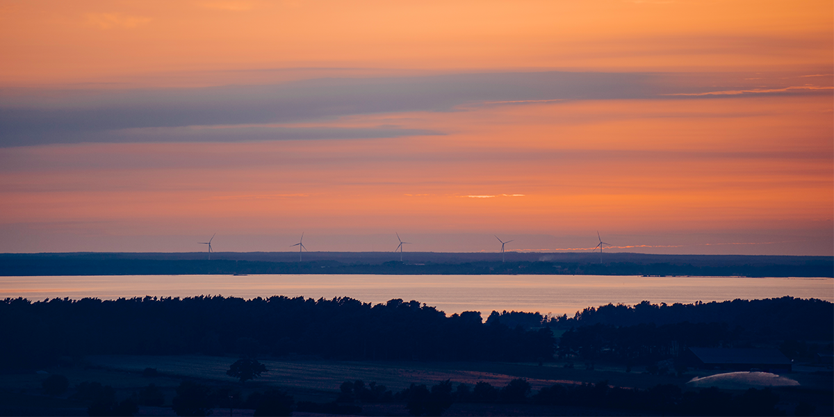 Solnedgång över Kalmar med vindkraftverk i horisontlinjen.
