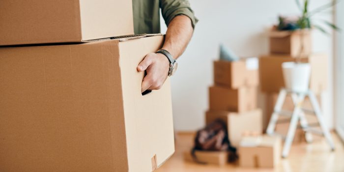 En person som håller i en flyttlåda. I bakgrunden ser man fler flyttkartonger staplade på varandra.