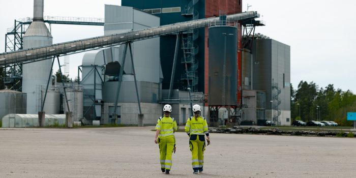 Två medarbetare i arbetskläder går över en öppen industriplan mot Kalmar Energis kraftvärmeverk i Moskogen.